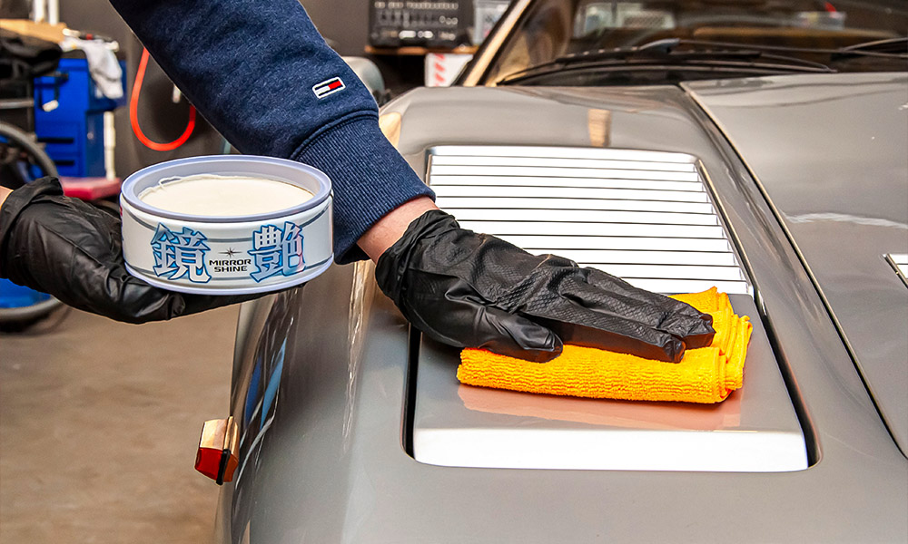 Photo of Soft99 car wax Mirror Shine being applied with a microfibre on a light silver Ferrari car.